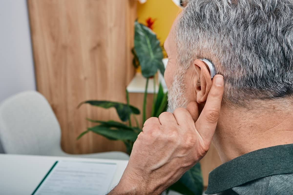 hearing aid on mans ear, as he adjust it