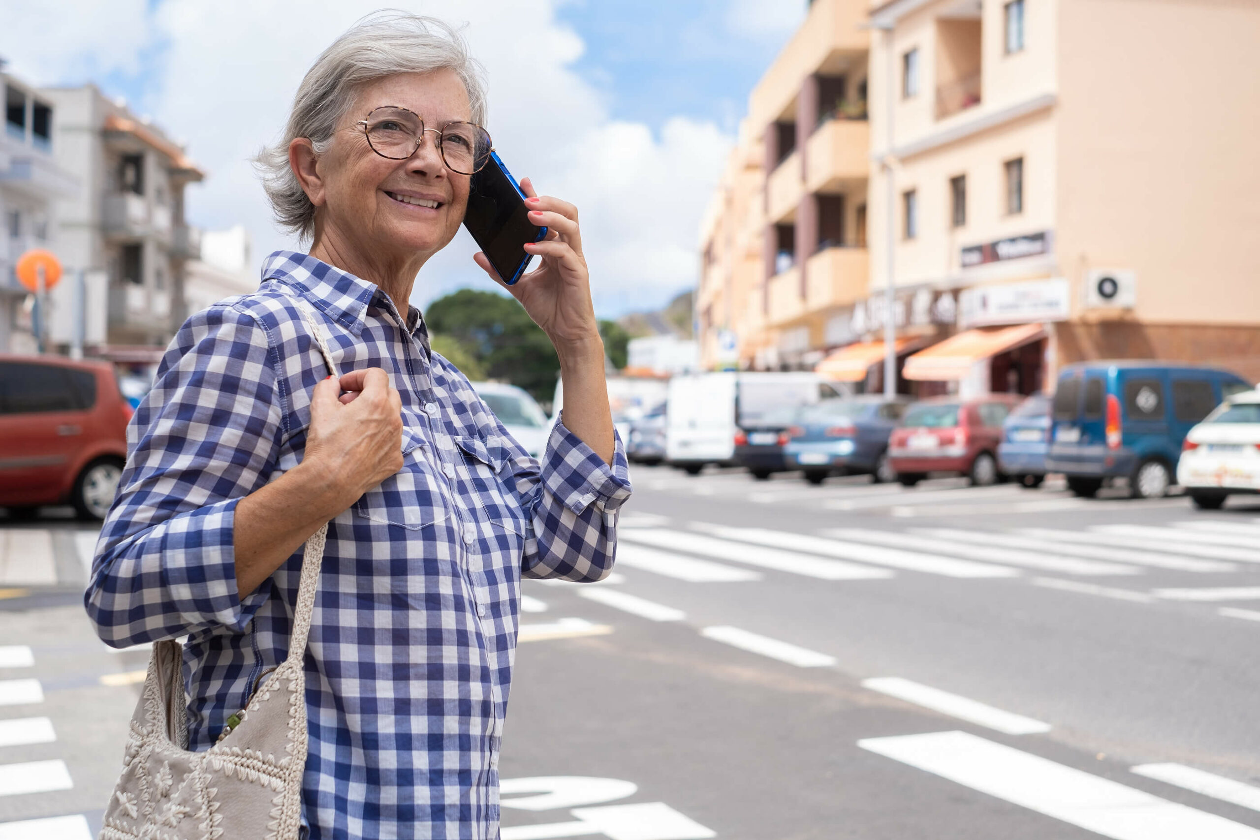 Older woman with hearing loss crossing a street with a smart phone up to her ear