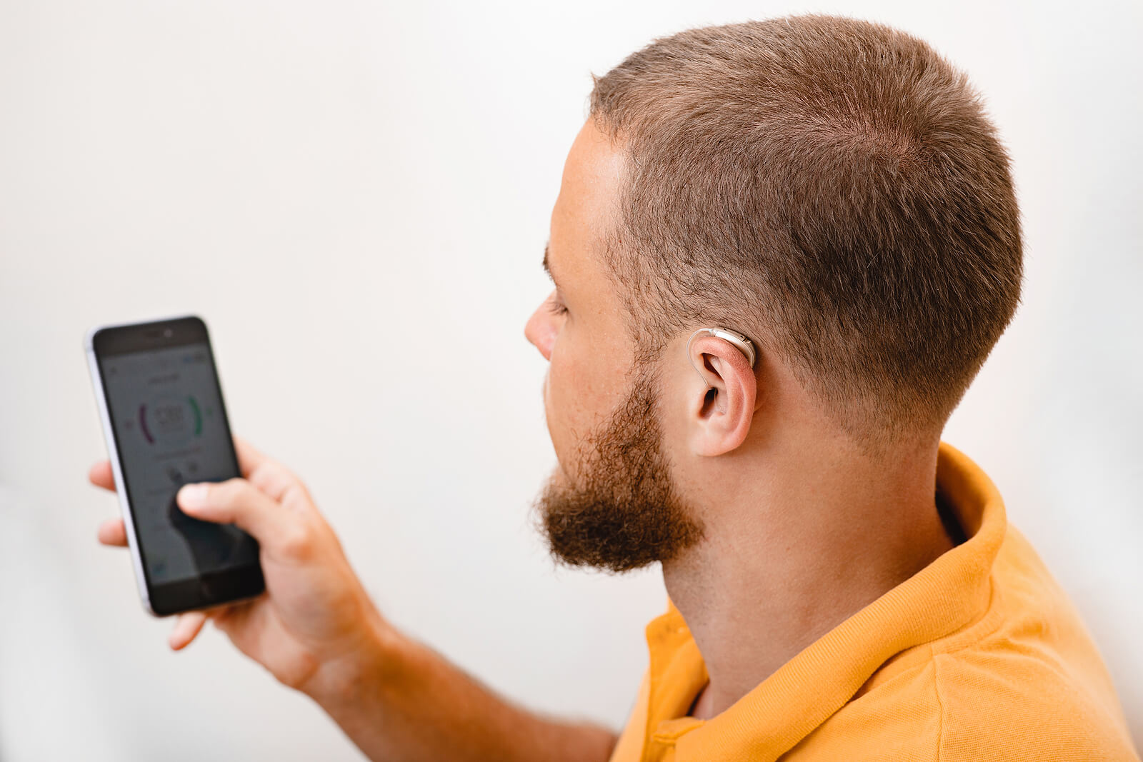 Man with hearing aid adjusting through cell phone app